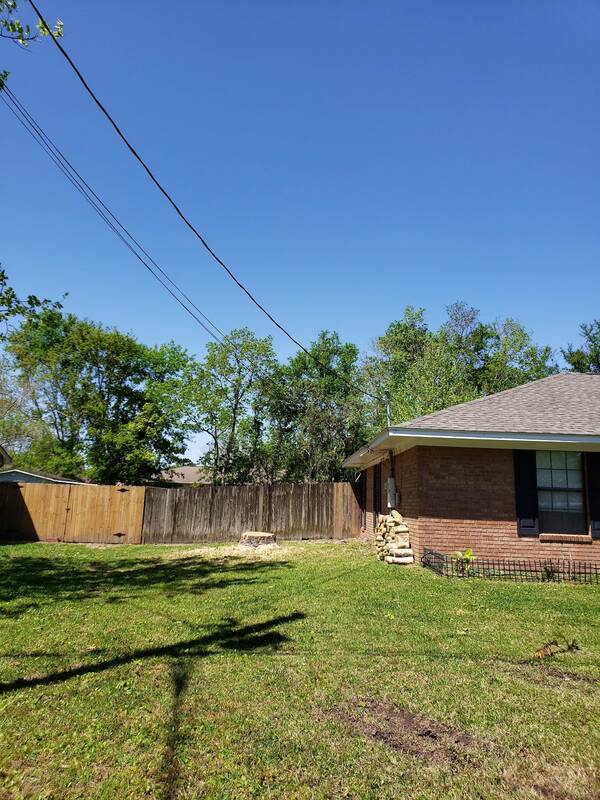 Open grass backyard of a brick house with a wooden fence and a small pile of cut wood rounds