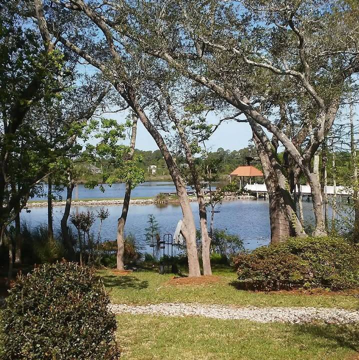 Live oaks on a mowed lawn with pine-straw beds and a lake behind